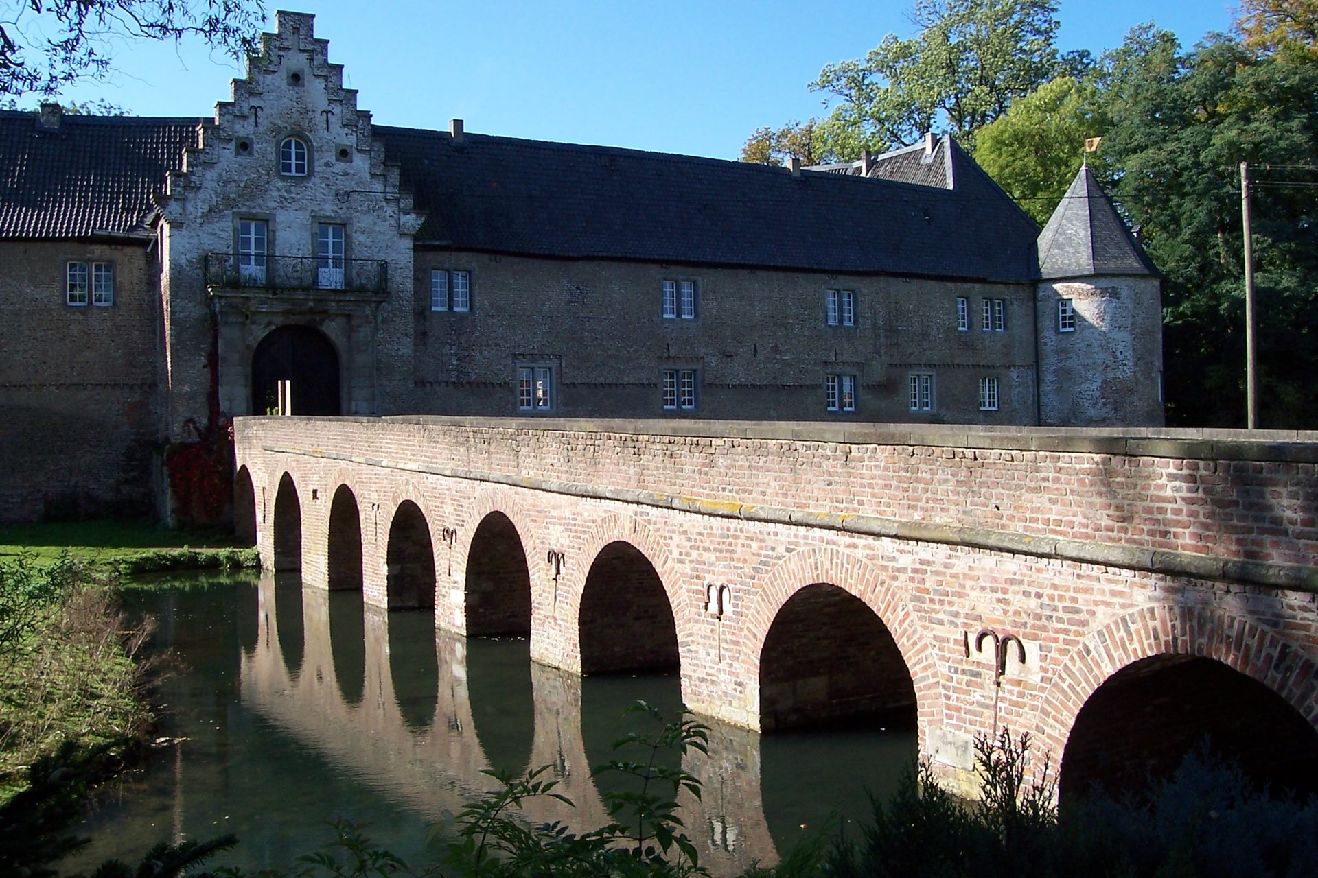 Schloss Hülchrath in Grevenbroich, die mittelalterliche Wasserburg mit steinerner Bogenbrücke über dem Burggraben, in dem sich das Torhaus mit dem Staffelgiebel spiegelt