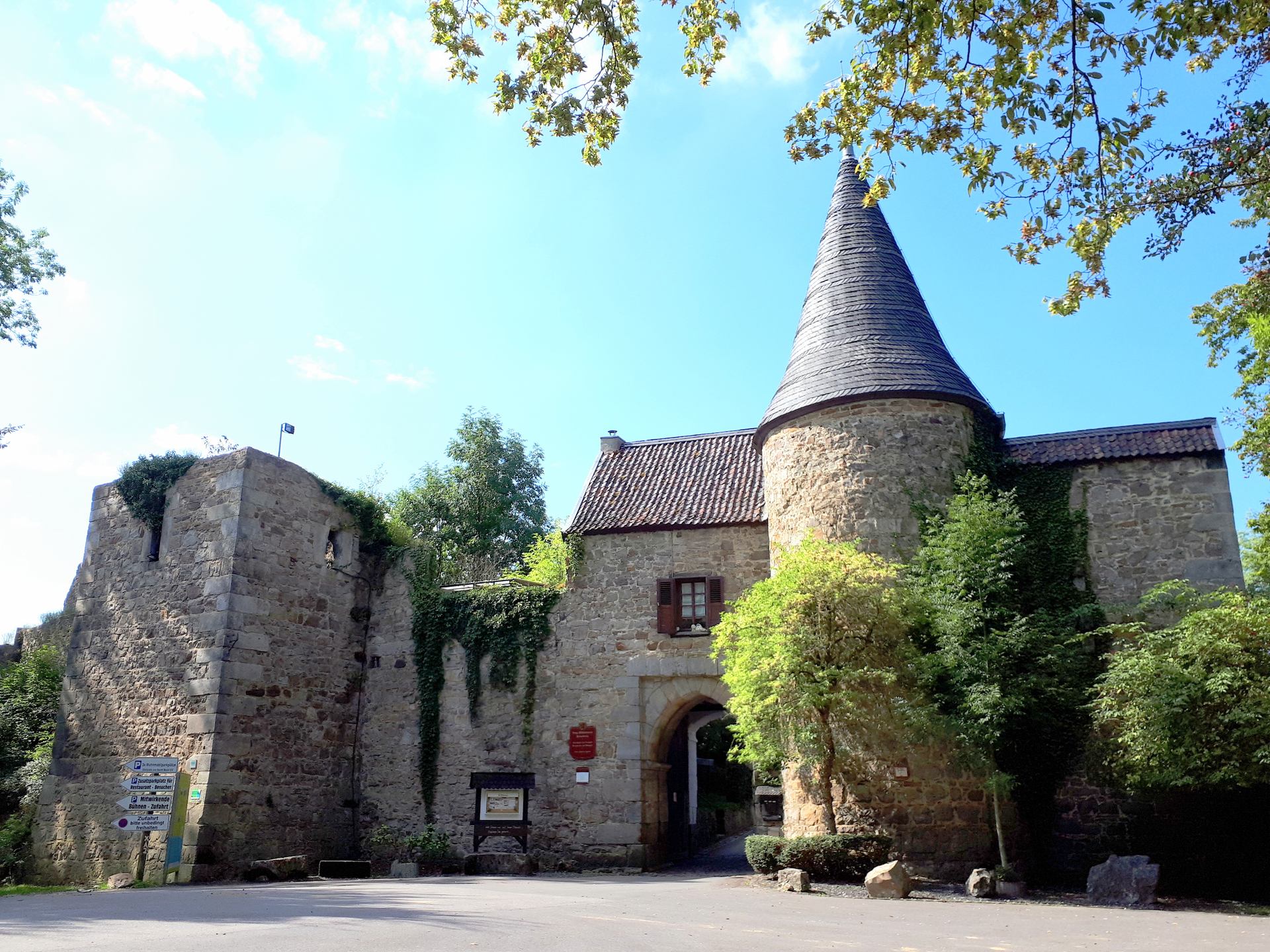 Burg Wilhelmstein in Würselen-Bardenberg, das mittelalterliche Torhaus mit spitzkegeligem Rundturm und efeubewachsenen Bruchsteinmauern unter blauem Himmel